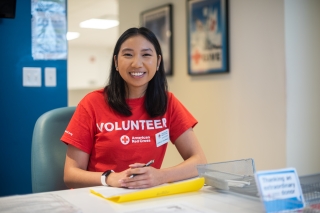 A smiling American Red Cross volunteer sitting at a table with paperwork and a pen in her hand